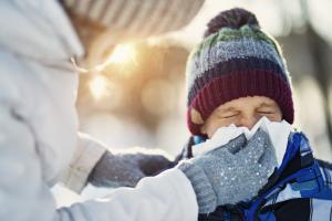 Parent holding a tissue up to a sneezing child suffering a common winter illness